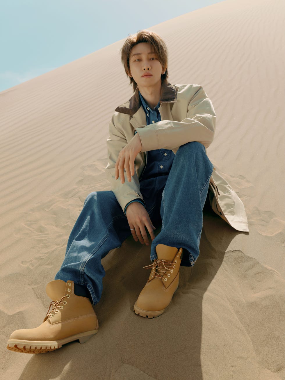 person sitting on sand wearing casual attire and boots
