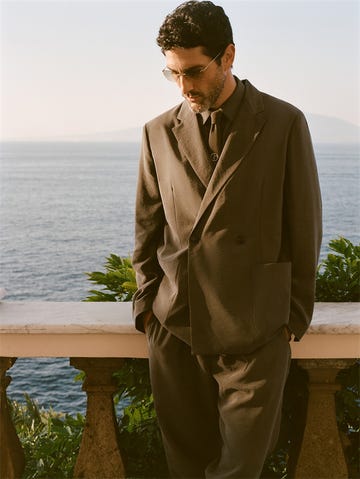 a man dressed in a tailored suit stands by a coastal view