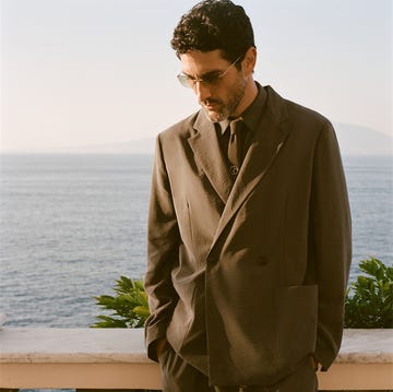 a man dressed in a tailored suit stands by a coastal view a man dressed in a tailored suit stands by a coastal view