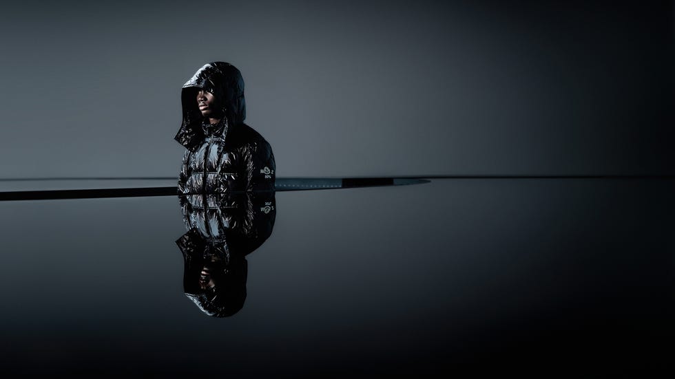a person dressed in a shiny black puffer jacket standing next to a reflective surface