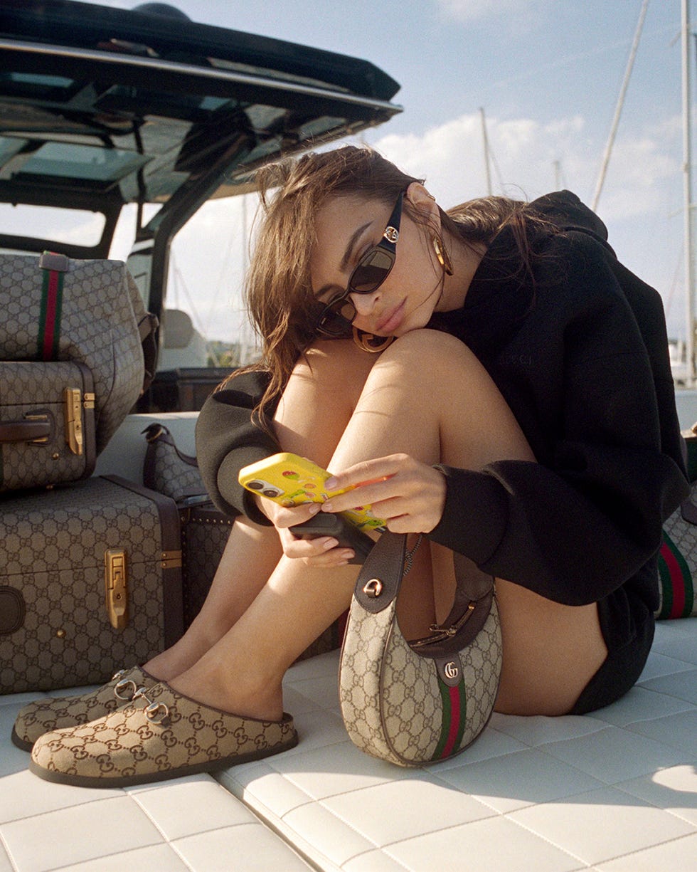a person seated on a boat deck interacting with a phone surrounded by designer items