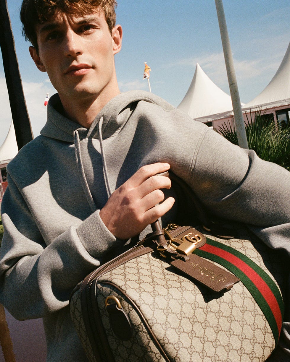a young person holding a designer bag while wearing a hoodie