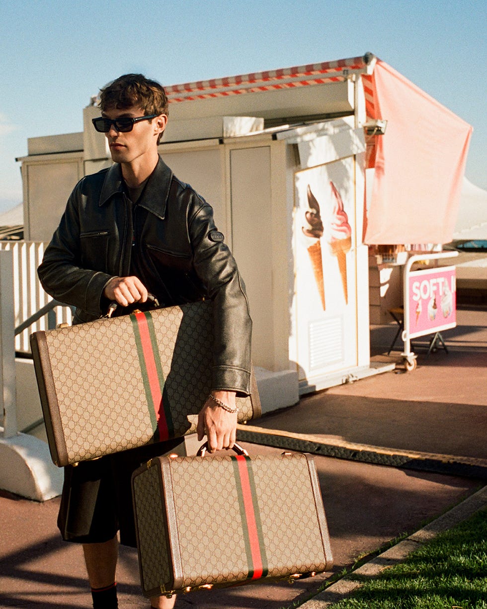 person carrying two gucci suitcases near an ice cream stand