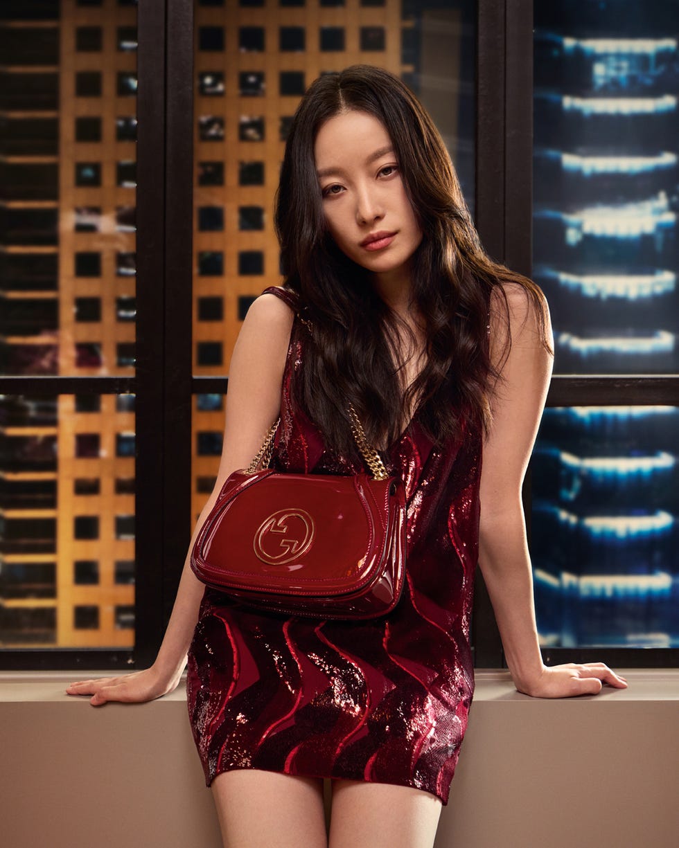 a person standing near a window wearing a sparkling red dress holding a designer handbag