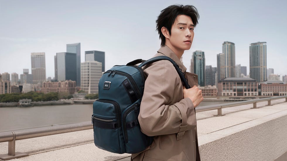 a person wearing a backpack while standing on a riverside promenade with a skyline in the background