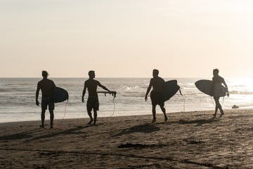 surfers walking along a beach at sunset