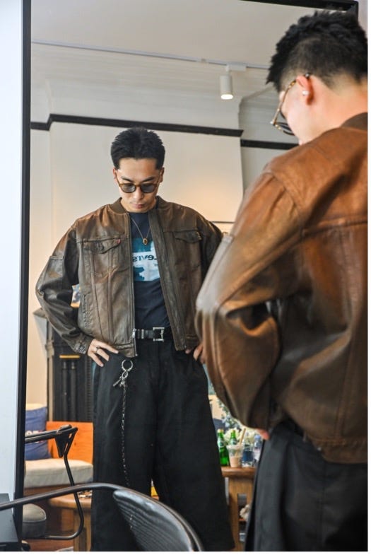 a person trying on a brown leather jacket and black pants while looking in a mirror