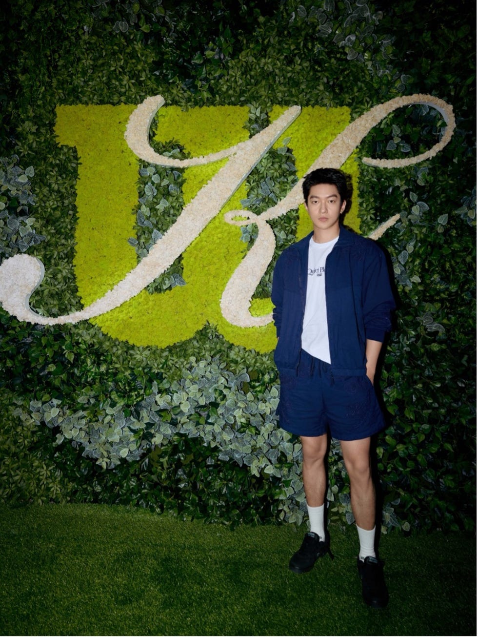 a person standing against a green wall featuring decorative plants and a large letter j