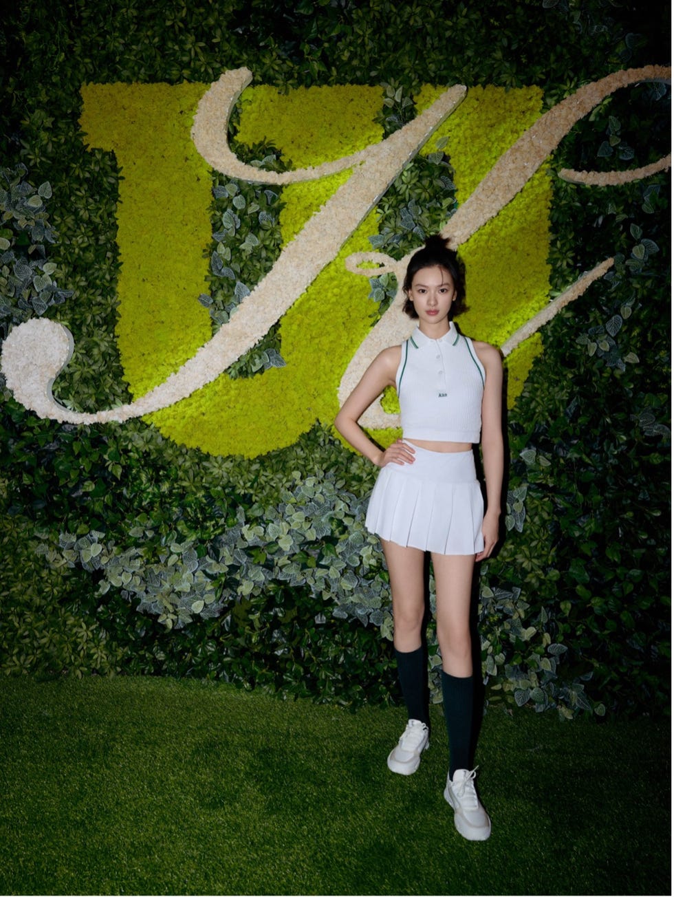 a person posing in front of a green wall adorned with a floral arrangement showcasing a stylized letter