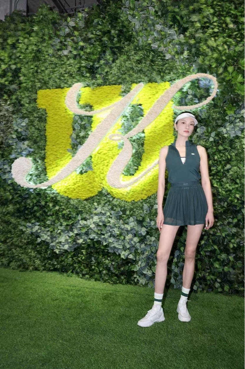 a model posed in front of a green wall display with a prominent logo