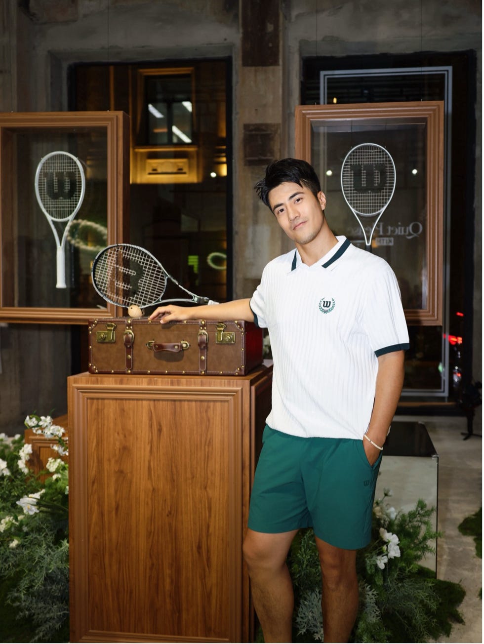 a male figure stands beside a wooden display with tennis equipment