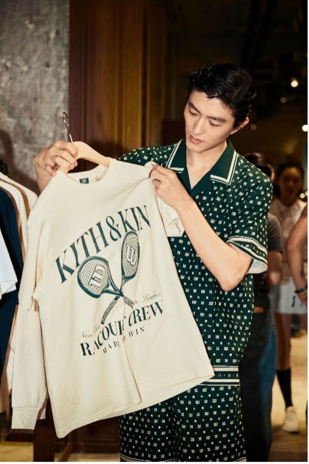 a person showcasing a creamcolored sweatshirt featuring the text kith kin and illustrations of tennis rackets