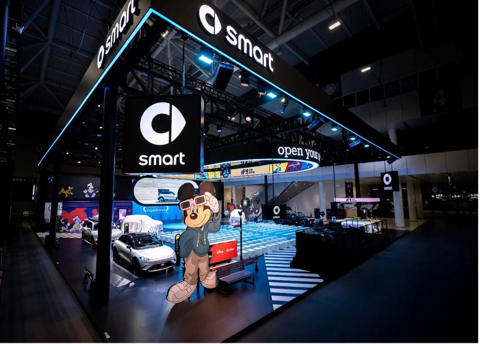 a exhibition of the new smart car with a mickey mouse standing next to it