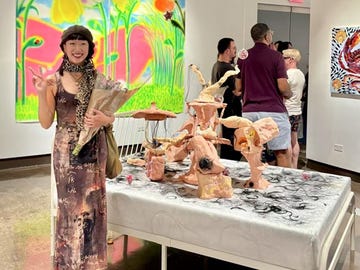 a woman holding flowers stands next to an art installation in a gallery