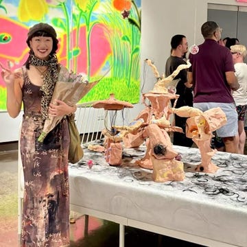 a woman holding flowers stands next to an art installation in a gallery a woman holding flowers stands next to an art installation in a gallery