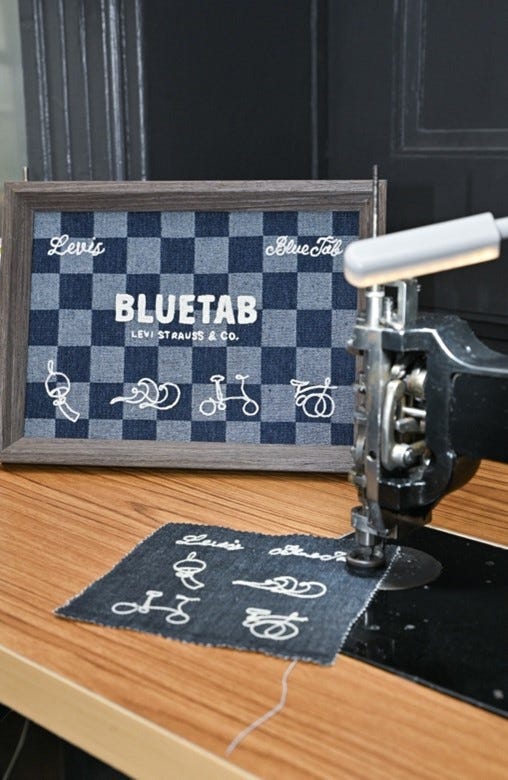 sewing machine beside a framed textile display featuring denim patterns and logos