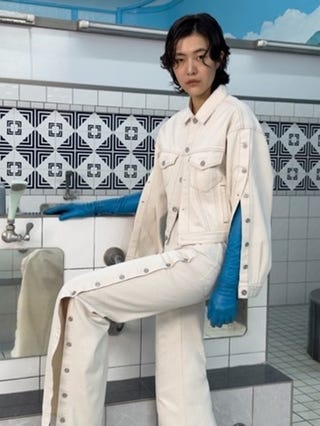 model wearing a white denim outfit with blue gloves in a tiled bathroom