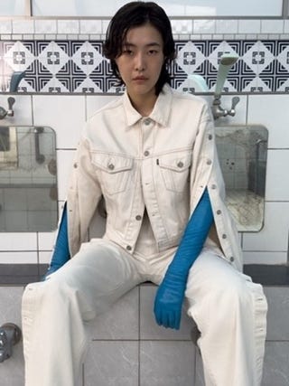 a person seated in a bathroom wearing a lightcolored outfit and blue gloves