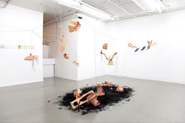 art installation featuring suspended organic forms and black hair on the floor