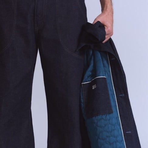 a model wearing dark denim pants and holding a jacket with a quilted inner lining