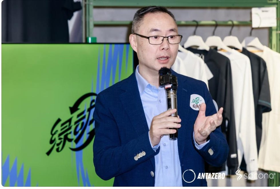 a person speaks at an event with a green backdrop and clothing display