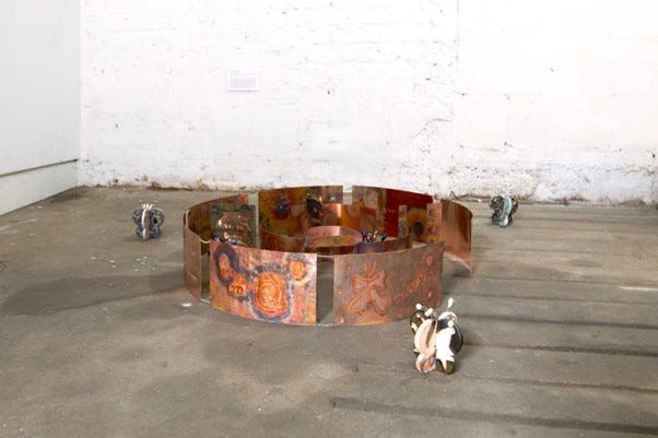sculptural installation featuring a circular metallic structure surrounded by small ceramic figures