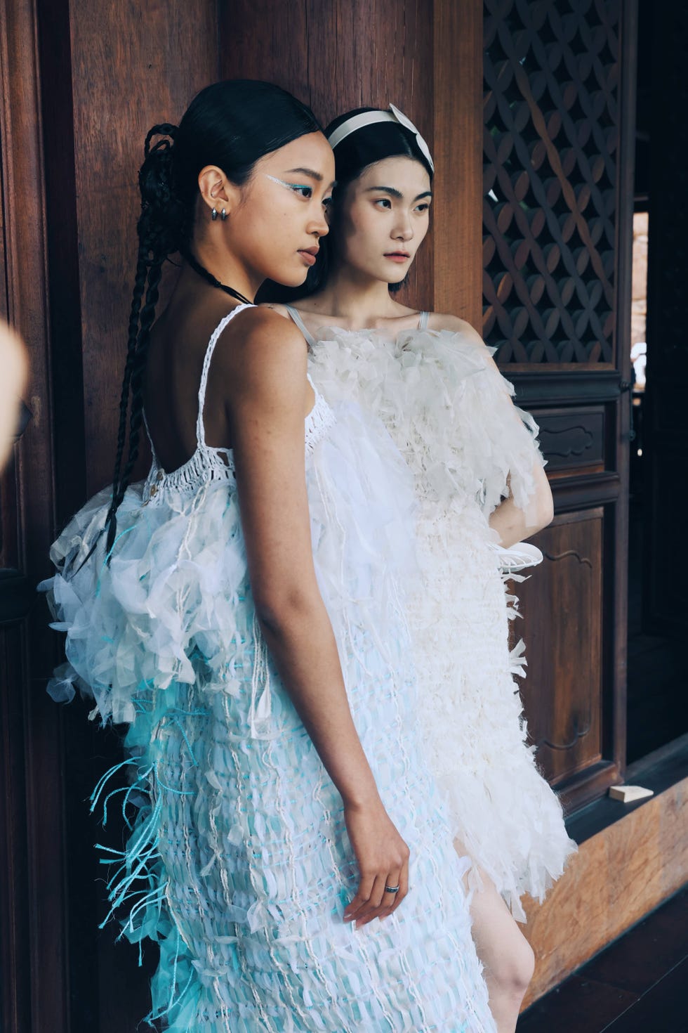 two models showcasing unique textured dresses in a wooden setting
