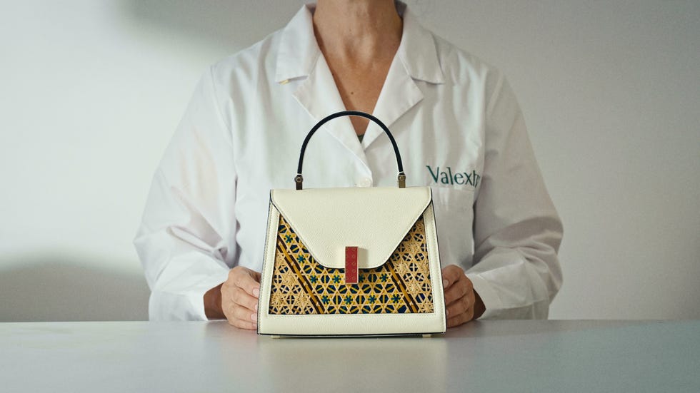 a stylish handbag displayed by a person wearing a lab coat