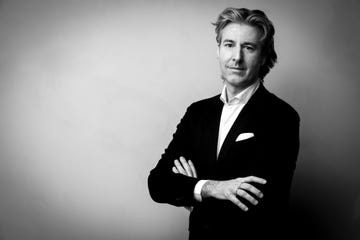 a person in a black suit with crossed arms facing the camera